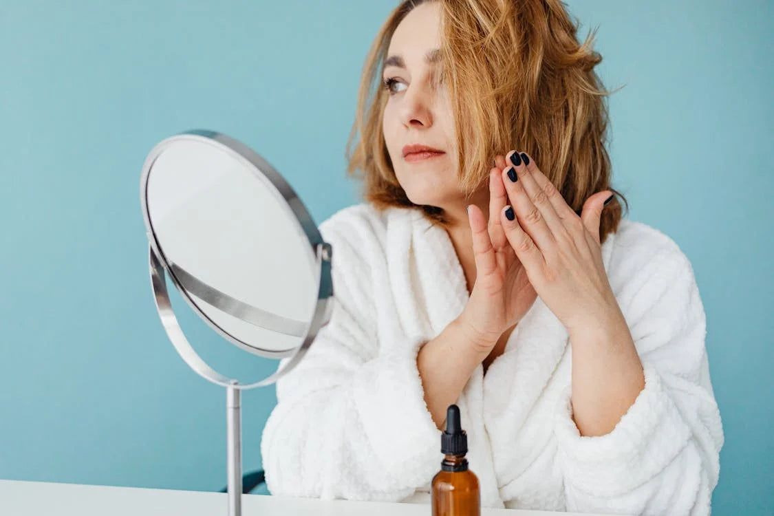 A woman in white robe rubbing essential oil on her hair