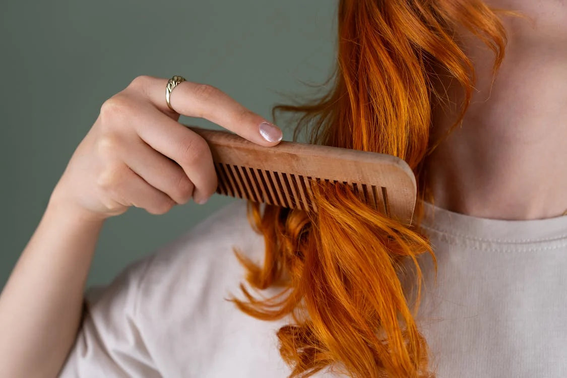 Woman combing vibrant red hair with wooden comb